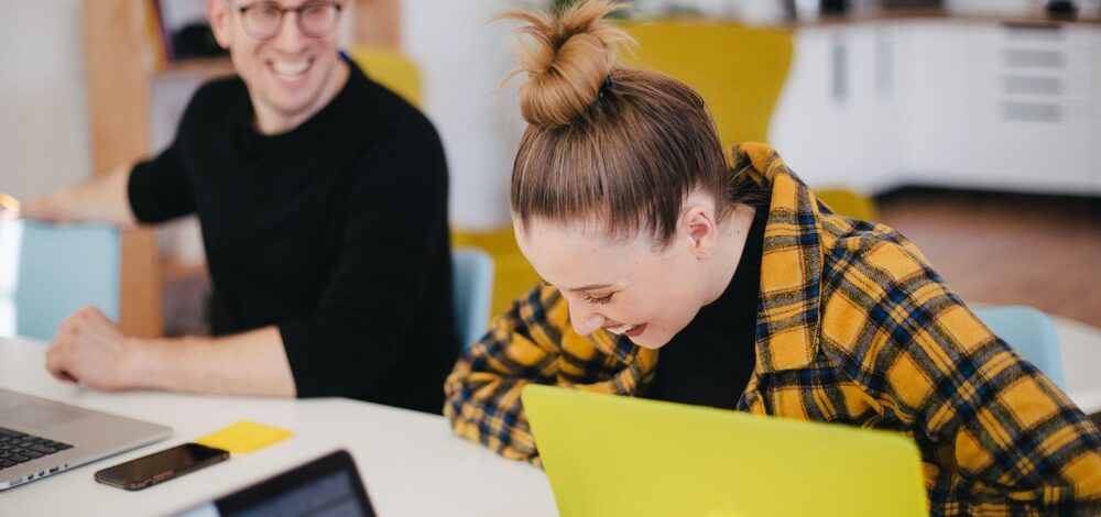 man and woman laughing while sitting in front of laptops