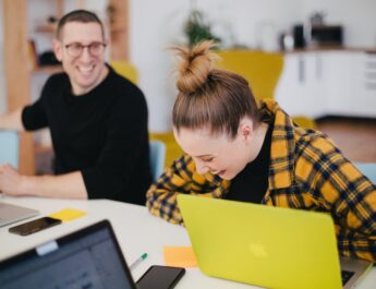 man and woman laughing while sitting in front of laptops